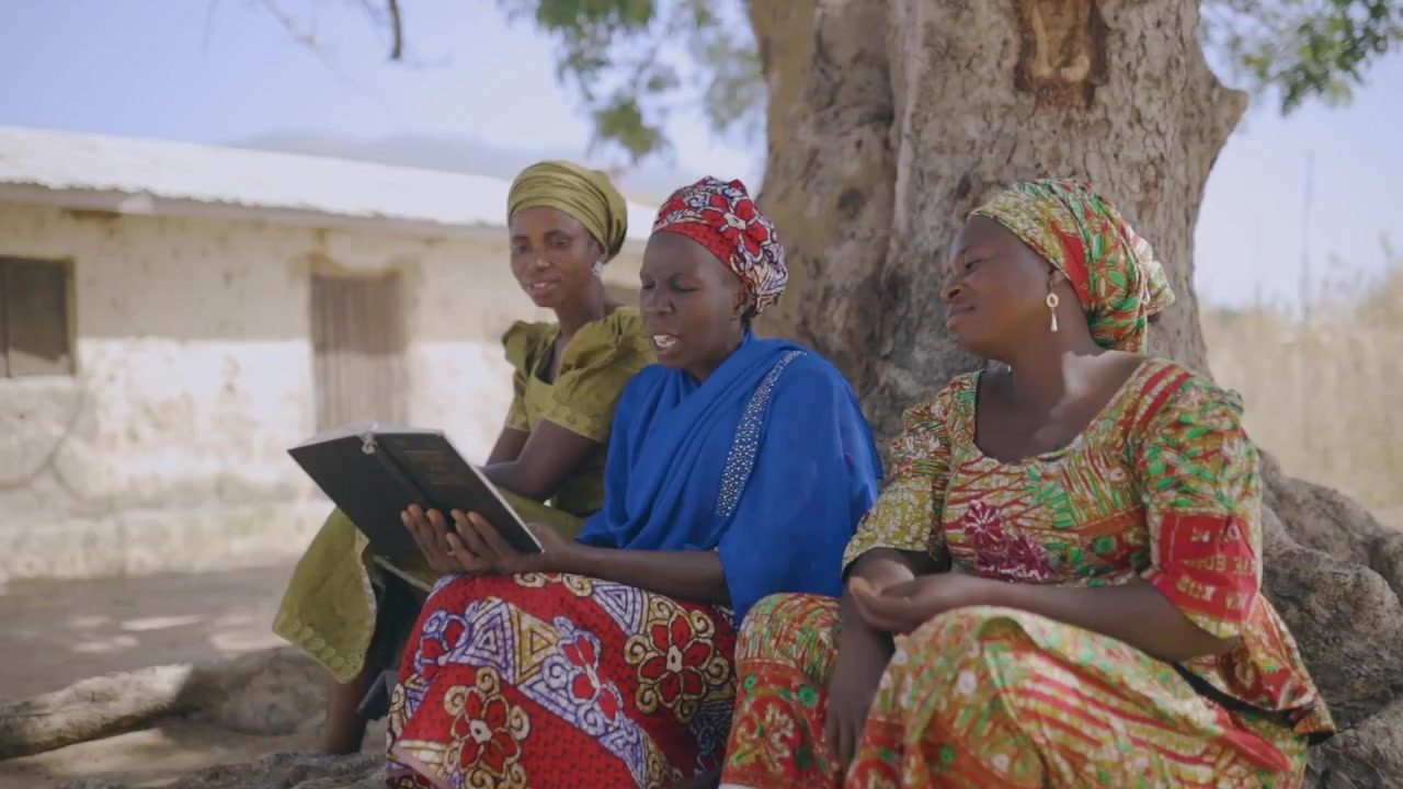 Women seated under a tree reviewing information on a tablet